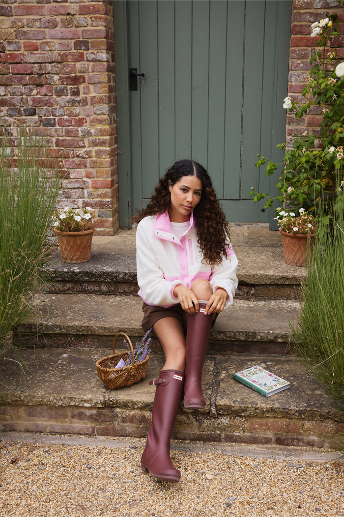 Model wearing Gym+Coffee Snap Polar Fleece Pink Blossom seated on garden steps Shop Gym+Coffee at Dotique
